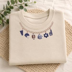 May include: A beige crewneck sweatshirt featuring an embroidered design of a gold chain necklace with charms. The charms include a megaphone, a football helmet, a football, a pom-pom, a flower, and a foam finger with the number 1 on it.
