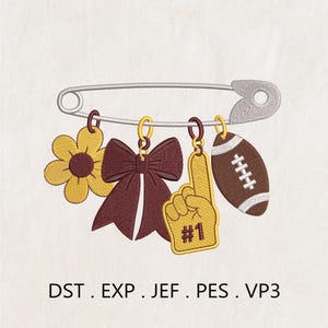May include: An embroidery design featuring a silver safety pin with four hanging charms: a yellow flower with a brown center, a maroon bow, a yellow foam finger with the text #1, and a brown football. Text below reads DST . EXP . JEF . PES . VP3.