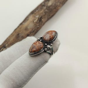 May include: A silver ring featuring two oval-shaped, brown and cream-colored stones. The stones are set in a decorative silver setting with a beaded border. The ring has a split shank design.