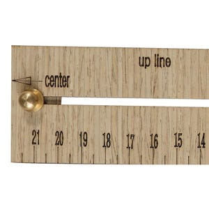 Op de afbeelding: Een houten ModulFit-liniaal met messing knoppen en een schuifmechanisme. De liniaal heeft metingen van 1 tot 21, met markeringen voor "up line", "center" en "side". De liniaal is lichtbruin met zwarte markeringen.