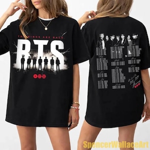 Könnte beinhalten: Ein schwarzes Kurzarm-T-Shirt mit Grafikdruck. Die Vorderseite zeigt den Text THE KINGS ARE BACK, das Wort BTS in großen weißen Buchstaben und die Silhouetten von sieben Figuren. Die Rückseite listet Tourdaten und Orte mit Gruppenfotos auf.