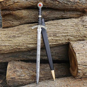 Può includere: Una spada in metallo color argento con impugnatura avvolta in nero, pomolo circolare con una pietra rossa e guardia decorata. La lama presenta intricati motivi incisi lungo la sua lunghezza. È incluso un fodero nero con punta in metallo dorato.