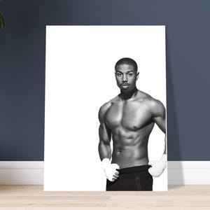 Puede incluir: Impresión en blanco y negro de una persona musculosa con pantalones deportivos negros y vendas blancas. La persona está de pie frente a un fondo blanco, con una pared azul oscuro y un suelo de madera visibles.