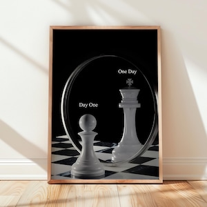 Peut inclure: Une affiche encadrée représentant un pion d'échecs blanc sur un damier noir et blanc. Un miroir circulaire derrière le pion reflète un roi d'échecs blanc. Le texte Day One est imprimé près du pion, et One Day est près du roi.
