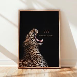 以下が含まれることがあります： 口を大きく開けたヒョウが描かれた、額縁入りの縦型ウォールアートプリント。背景は無地の黒で、右上のスペースには222とThe world is yours.という文字が明るいゴールドカラーでプリントされています。