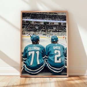 Könnte beinhalten: Ein gerahmtes Foto zeigt zwei Eishockeyspieler von hinten, die türkisfarbene Trikots mit weißen Akzenten tragen. Der linke Spieler trägt CELEBRINI und die Nummer 71, der rechte Spieler SMITH und die Nummer 2. Beide tragen türkisfarbene Helme auf dem Eis.