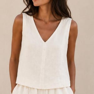 Puede incluir: Un conjunto de dos piezas compuesto por una blusa sin mangas con cuello en V y pantalones anchos a juego en color blanco roto. La blusa presenta un cierre frontal de botones, mientras que los pantalones tienen un corte relajado con cintura el&aacute;stica.