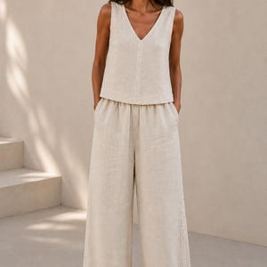 Puede incluir: Un top beige sin mangas con escote en V combinado con pantalones anchos a juego. El conjunto est&aacute; confeccionado en un tejido texturizado de color tostado claro neutro, con un corte relajado y una silueta limpia y sencilla sin estampados.