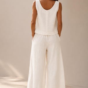 Puede incluir: Un conjunto de dos piezas que consta de una parte superior sin mangas con cuello redondo y pantalones a juego de pierna ancha. Las prendas est&aacute;n confeccionadas en una tela de color blanco roto con un tejido texturizado visible. La parte superior tiene un dobladillo recto.