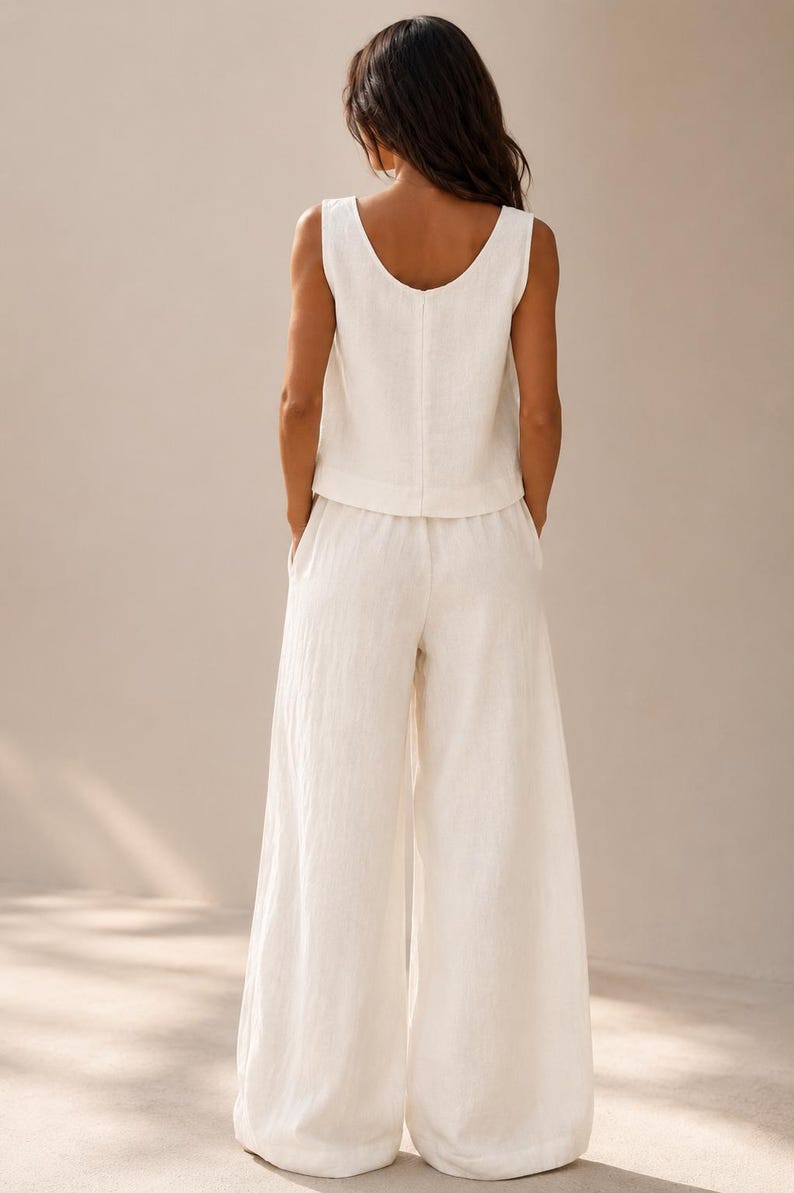 Puede incluir: Un conjunto de dos piezas que consta de una parte superior sin mangas con cuello redondo y pantalones a juego de pierna ancha. Las prendas est&aacute;n confeccionadas en una tela de color blanco roto con un tejido texturizado visible. La parte superior tiene un dobladillo recto.