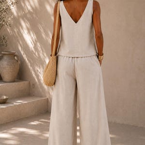 Puede incluir: Un conjunto de dos piezas en color beige compuesto por una blusa sin mangas con cuello en V y pantalones de pierna ancha. El conjunto est&aacute; confeccionado en un tejido texturizado de tono neutro. Incluye un bolso de hombro de paja trenzada.