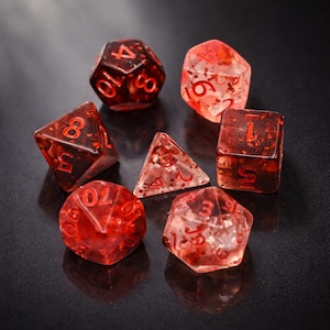 May include: A collection of seven polyhedral dice in red and clear hues. The dice are made of a translucent material with red flecks, and the numbers are painted in red. These dice are for tabletop role-playing games.