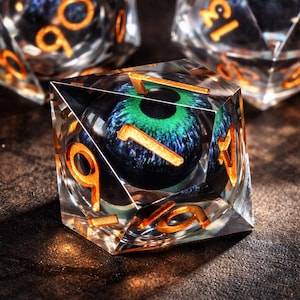 Puede incluir: Un dado transparente, multifacético con números dorados. El dado presenta un diseño detallado en forma de ojo con tonos verdes y azules. El diseño del ojo está centrado dentro del dado, creando un efecto visual único. Otros dados son visibles en el fondo.