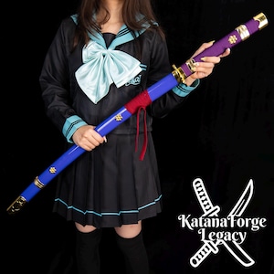 Könnte beinhalten: Ein blau-violettes Katana mit goldenen Akzenten. Der Griff ist mit violettem Stoff umwickelt, und die Klinge ist blau. Das Katana hat goldene Verzierungen und einen rot umwickelten Abschnitt. Das Bild enthält den Text "Katana Forge Legacy".