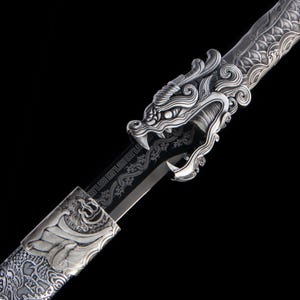 Puede incluir: Una espada de tono plateado con una empuñadura detallada en forma de cabeza de dragón y una vaina con intrincados patrones en relieve. La hoja muestra una superficie oscura y reflectante con diseños geométricos y serpentinos grabados.