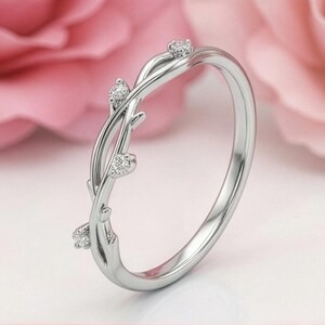 May include: A silver-coloured ring featuring a band designed to resemble intertwined vines or branches. The band is accented with four small, clear, sparkling stones set at intervals along the twisted metal structure, creating a delicate and organic appearance.