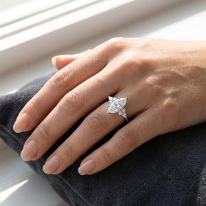 以下が含まれることがあります： 銀色のリングで、中央に大きなマーキスカットの石が配置され、その両側に2つずつ小さな三角形のカット石が並んでいます。細い金属製のバンドにセットされており、透明なファセットカットの石が左右対称に配置されたデザインです。