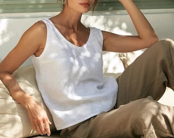 May include: A sleeveless white top with a scoop neckline and a relaxed fit, paired with loose-fitting tan trousers. The top features a simple, clean design with wide shoulder straps and a straight hemline, crafted from a lightweight, textured fabric.