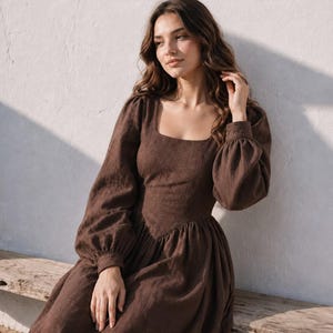May include: A long-sleeved brown dress featuring a square neckline, a fitted bodice with a pointed waistline, and a full, gathered skirt. The sleeves are voluminous with fitted cuffs, and the garment is constructed from a textured fabric.