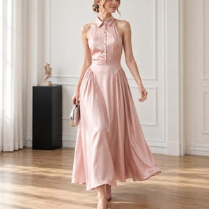 May include: A dusty rose satin midi dress featuring a sleeveless halter neckline with a classic collar, a button-down bodice, and a pleated skirt that falls to a mid-calf length. The garment is paired with matching pointed-toe heels and a small clutch.