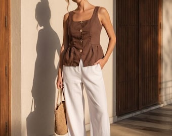 May include: A sleeveless brown peplum top with a square neckline and four front buttons, paired with wide-leg white trousers. The outfit is accessorized with a woven straw handbag and simple white thong sandals, creating a clean ensemble.