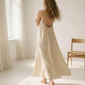 May include: A floor-length, beige, sleeveless dress with thin shoulder straps and a low-cut back. The garment features a loose, flowing silhouette that reaches the ankles, crafted from a textured fabric with a simple, unadorned design.