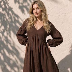 May include: A dark brown midi dress featuring a deep V-neckline, long voluminous sleeves with gathered cuffs, and a fitted bodice that transitions into a full, flowing skirt. The garment is constructed from a solid-colored fabric with a visible texture.