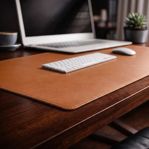 Peut inclure: Un sous-main rectangulaire en cuir beige avec des coins arrondis et des coutures visibles sur les bords. Le tapis est posé sur une surface en bois sombre, offrant un espace de travail plat et lisse pour un clavier et une souris d'ordinateur blancs.