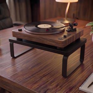 May include: A wooden record player with a black vinyl disc sits on a black metal stand. The turntable features a tonearm with a red cartridge, a circular platter, and a control slider on the top surface. The stand has four legs.