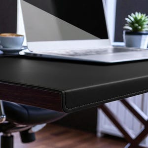 May include: A black leather desk with a dark wood trim and a laptop computer. A cup of coffee and a small potted plant are also visible. The desk is part of a home office setup.