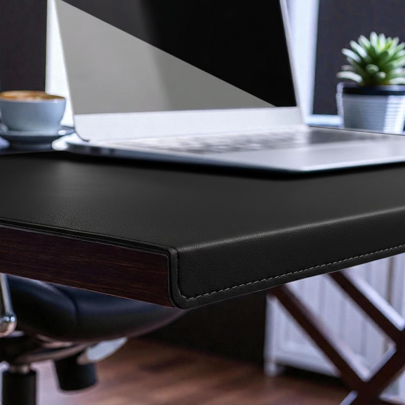 May include: A black leather desk with a dark wood trim and a laptop computer. A cup of coffee and a small potted plant are also visible. The desk is part of a home office setup.
