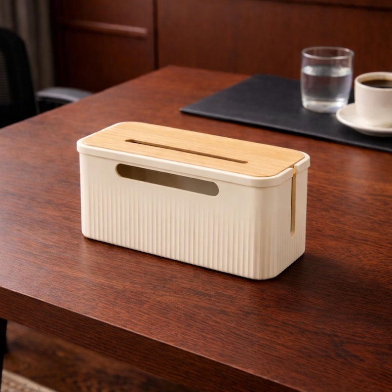 May include: A cream-colored rectangular cable organizer with a light wood grain lid. The organizer has a slot on top and a curved opening on the side. The ribbed texture on the front adds a decorative element. The organizer sits on a dark wood surface.