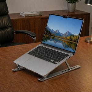 May include: A silver laptop computer is propped up on an adjustable silver laptop stand on a wooden desk. The laptop screen displays a scenic mountain and lake view. The stand is designed to elevate the laptop for ergonomic use.