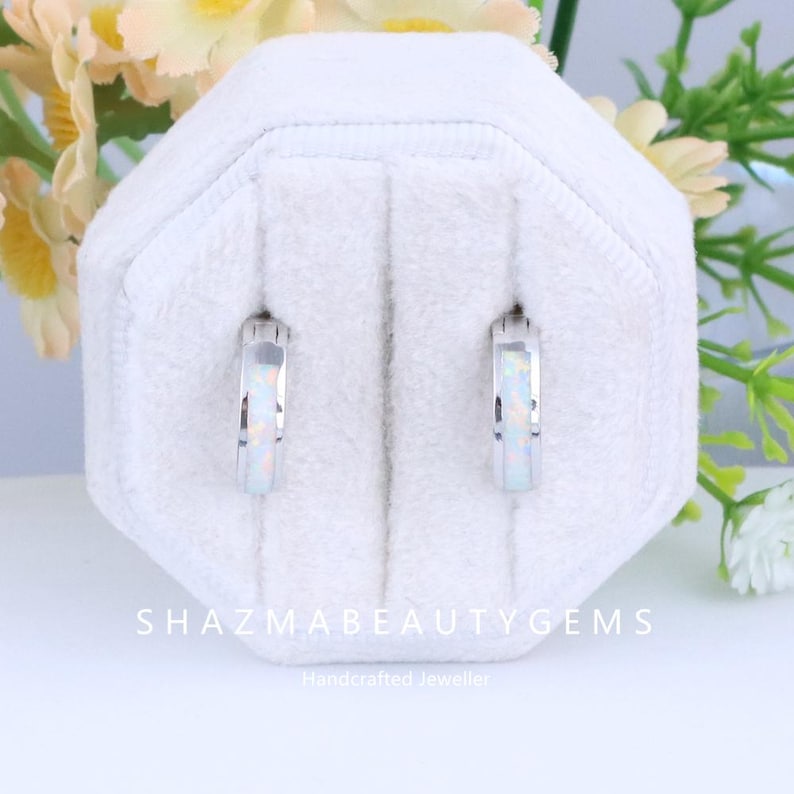 May include: A pair of small, silver hoop earrings with a white opal inlay. The earrings are displayed in a white jewelry box. The text "SHAZMABEAUTYGEMS" and "Handcrafted Jeweller" are visible.