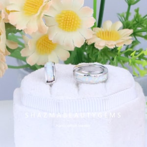 May include: A pair of silver-toned hoop earrings and a matching ring, both inlaid with a white opal-like material. The jewelry is displayed on a white surface with the text "SHAZMABEAUTYGEMS" and "Handcrafted Jeweller".