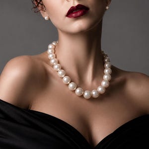Puede incluir: Un collar de una sola hilera con perlas grandes, redondas y de color crema de tamaño uniforme. El collar se combina con pendientes de perlas a juego. Las perlas tienen un acabado liso y brillante, ensartadas alrededor del cuello.