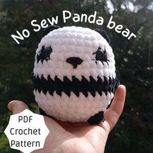 Pode incluir: Um urso panda de crochê feito à mão, predominantemente branco com detalhes pretos nas orelhas, olhos, nariz e corpo. O texto "No Sew Panda bear" está acima do panda e "PDF Crochet Pattern" está abaixo.