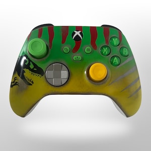 May include: Custom-painted Xbox controller with a Jurassic Park theme. The controller has a green, yellow, and red colour scheme with a dinosaur silhouette and the iconic logo. The buttons are green, yellow, and grey.