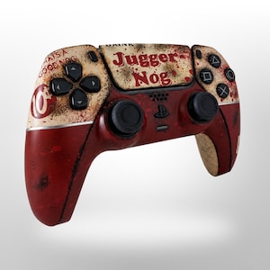 May include: A custom PlayStation 5 controller with a distressed, vintage design. The controller features a red and cream color scheme with the words "Juggernog" and "Whats a Good Nog" printed on it. The buttons and joysticks are black.