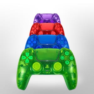 Peut inclure: Une pile de quatre manettes de jeu sans fil à la finition translucide, disposées de haut en bas en violet, rouge, bleu et vert. Chaque manette comprend un pavé tactile central, deux joysticks analogiques, une croix directionnelle et des boutons.