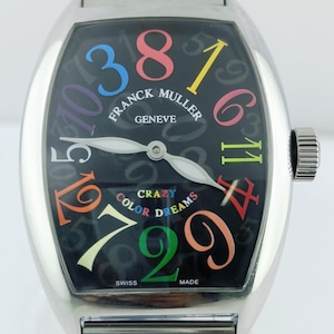 May include: A stainless steel Franck Muller Geneve watch with a black face. The watch face features colorful numerals and the words "CRAZY COLOR DREAMS". The watch has a silver band and a crown on the side.