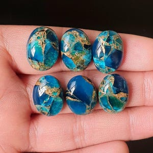 Op de afbeelding: Zes ovale edelstenen met een mozaïekpatroon van turquoise, blauw en goud. De gepolijste stenen worden tegen een donkere achtergrond gepresenteerd. Deze edelstenen zijn waarschijnlijk bedoeld voor het maken van sieraden of ambachten.