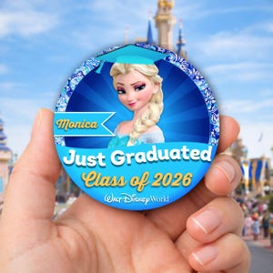 Peut inclure: Un bouton de graduation rond et bleu avec Elsa de La Reine des Neiges de Disney. Le bouton indique "Monica Just Graduated Class of 2026" avec le logo Walt Disney World. Le fond montre un ciel bleu et un château Disney.