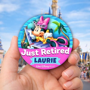 May include: A round, pink and blue button featuring Minnie Mouse relaxing on a beach chair. The text "Just Retired LAURIE Walt Disney World" is displayed on the button. The background shows a sunny day at a theme park.