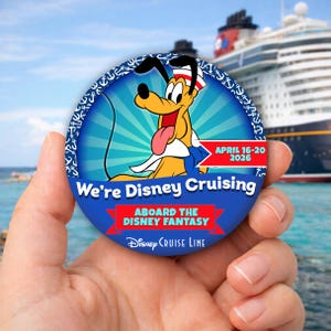Puede incluir: Un botón redondo azul con Pluto de Disney. El botón tiene el texto "We're Disney Cruising" y "April 16-20 2026". El fondo muestra un crucero y el mar.
