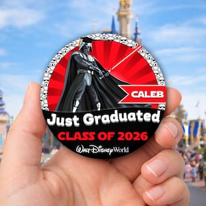 May include: A round graduation button featuring Darth Vader with a red lightsaber, wearing a graduation cap. The button has the text "Just Graduated", "Class of 2026", and "Caleb" with the Walt Disney World logo. The background is a red burst.