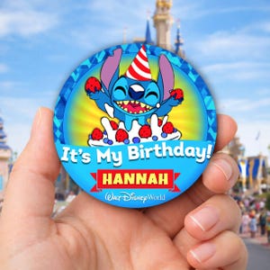 May include: A round blue button featuring the character Stitch from Disney's Lilo & Stitch, wearing a party hat and holding strawberries. The text "It's My Birthday!" and the name "HANNAH" are displayed on the button, along with the Walt Disney World logo.