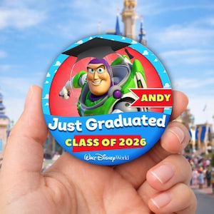 May include: A round button featuring Buzz Lightyear in a graduation cap. The button has a blue border with the text "Just Graduated CLASS OF 2026" and "ANDY". The Walt Disney World logo is at the bottom.