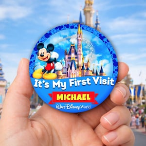 Puede incluir: Un botón redondo azul con Mickey Mouse, un castillo y el texto "It's My First Visit" con el nombre "MICHAEL" en una pancarta roja. El botón también incluye el logotipo de "Walt Disney World".