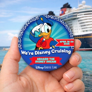 Pode incluir: Um botão redondo azul com o Pato Donald a saudar, com o texto "We're Disney Cruising" e "Aboard the Disney Dream". O botão também inclui as datas "April 16-20 2026" e o logotipo da Disney Cruise Line.